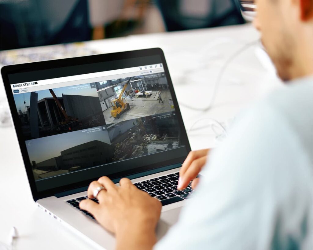 Close-up of a laptop screen featuring the cloud-based time-lapse software. The interface displays multiple live feeds from construction sites, highlighting the remote surveillance and analytical capabilities of the system.